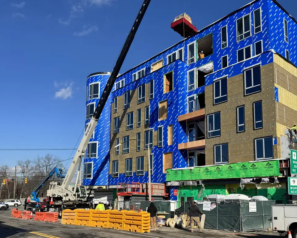 DJ Snyder crane, with Snyder on the boom, lifting a rooftop HVAC unit onto a five-storey building under construction